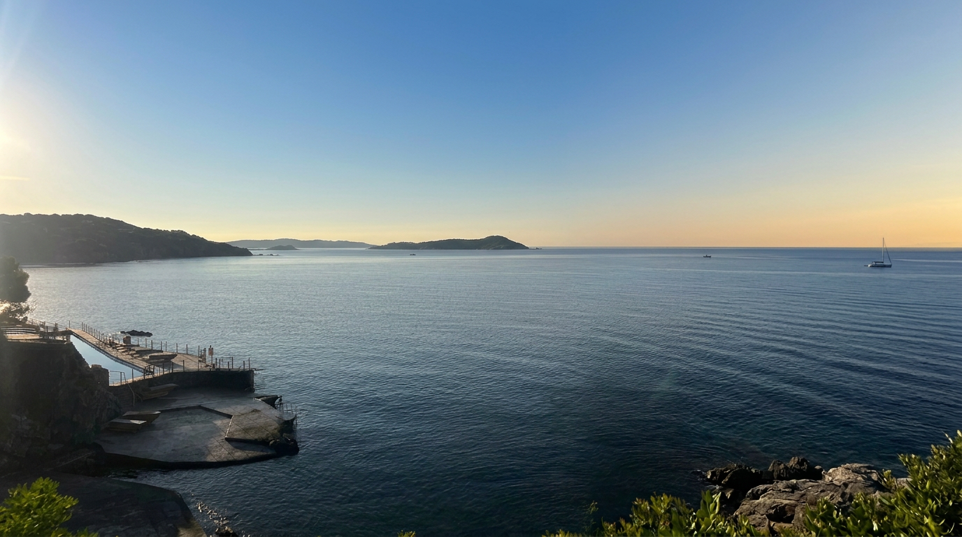 Vue panoramique sur une mer calme au coucher du soleil, avec des îles lointaines et un petit quai en bois.